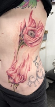 Water color tattoo on rib cage coming from hip, red and pink tones, by don art in motion tattoo shop.